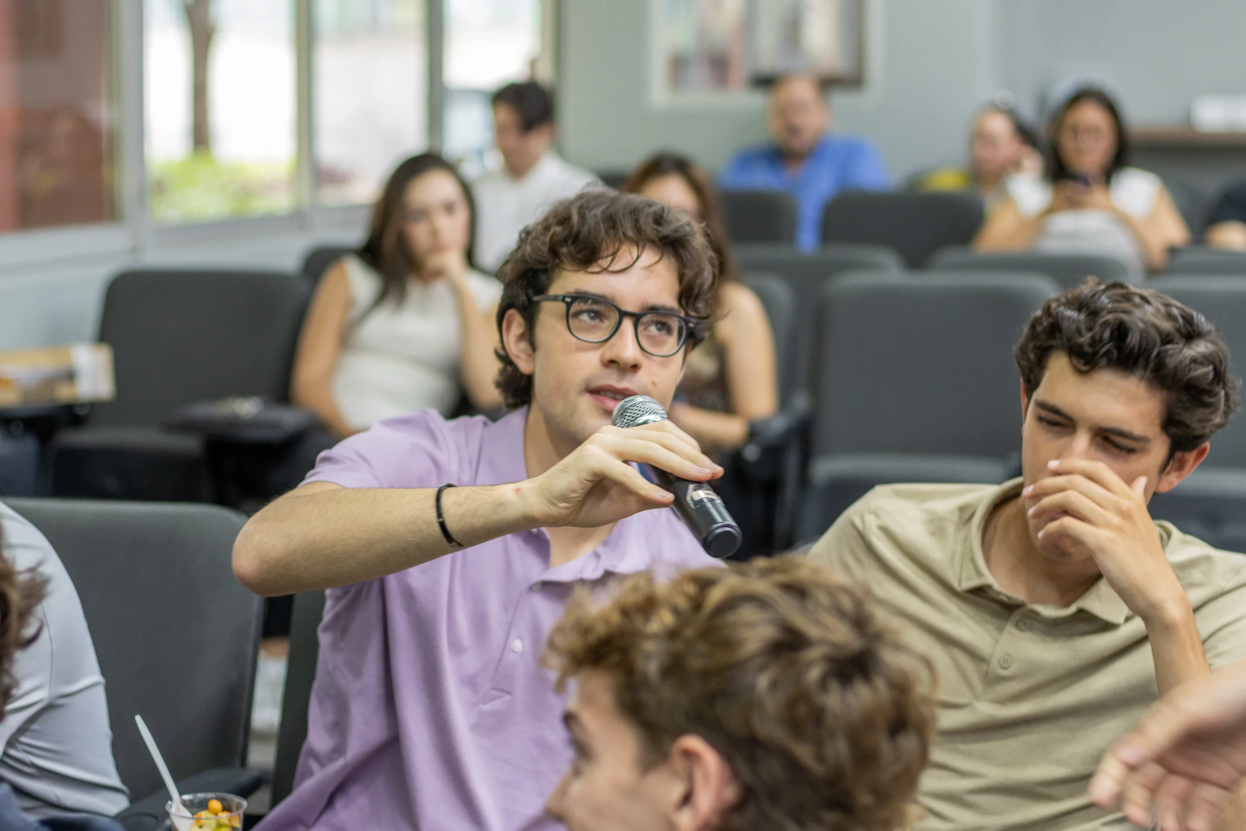 Estudiante de la FLDM con micrófono haciendo una pregunta durante una clase, con compañeros escuchando alrededor