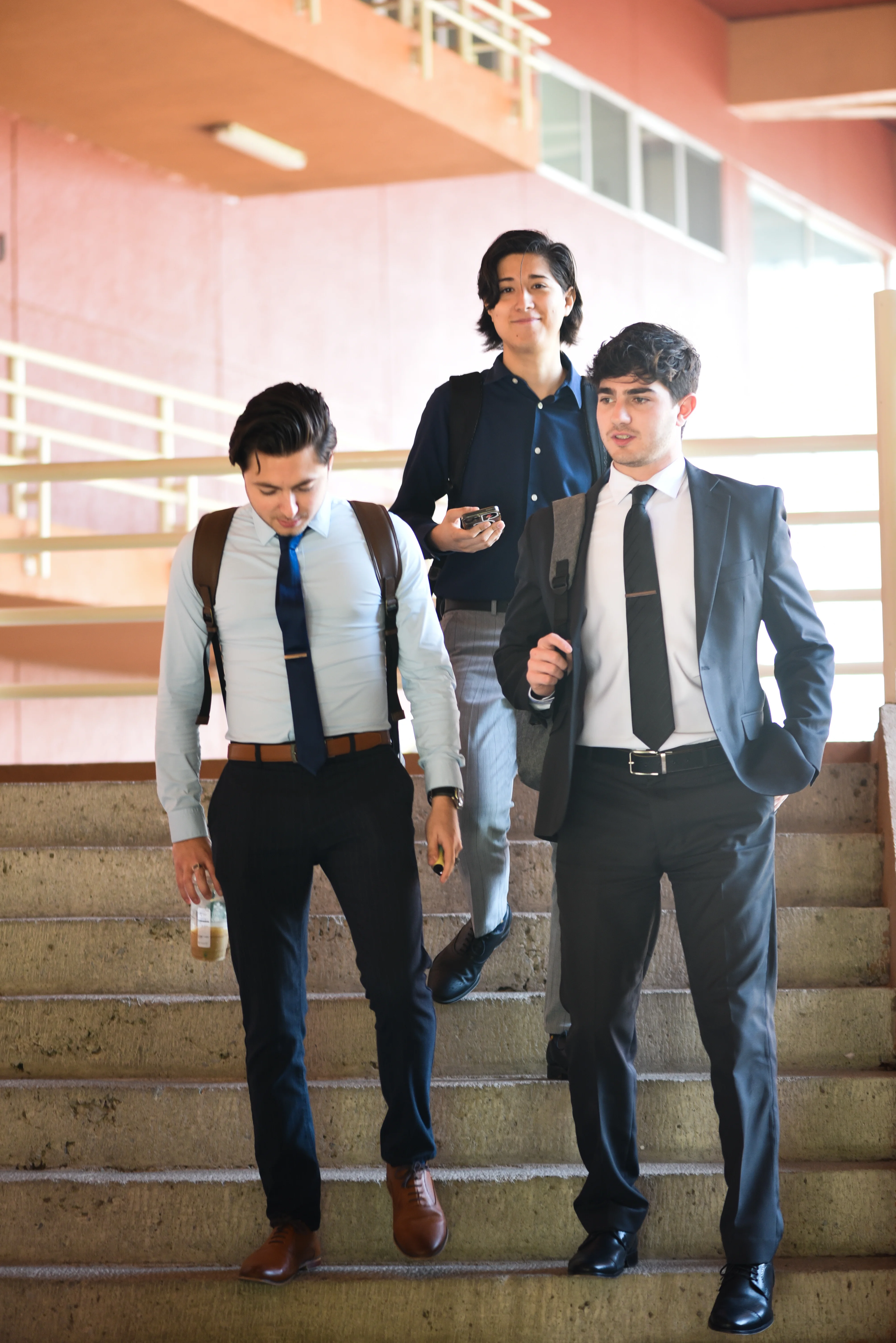 Tres estudiantes de la FLDM con traje bajan una escalera conversando entre clases